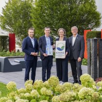 Matthias Hausmann von der IHK Schwaben (links) übergibt im Beisein des stellvertretenden Landrats Martin Stegmair (rechts) die EMAS-Urkunde an Roland Handschiegel und Stine Blinne von Hama.